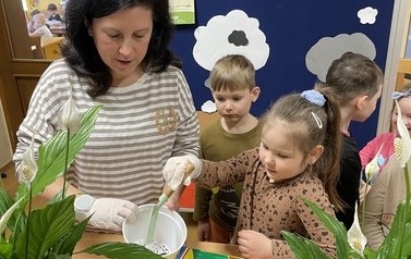 Dziewczynka wsypuje ziemię do doniczki, kt&oacute;rą trzyma pani.